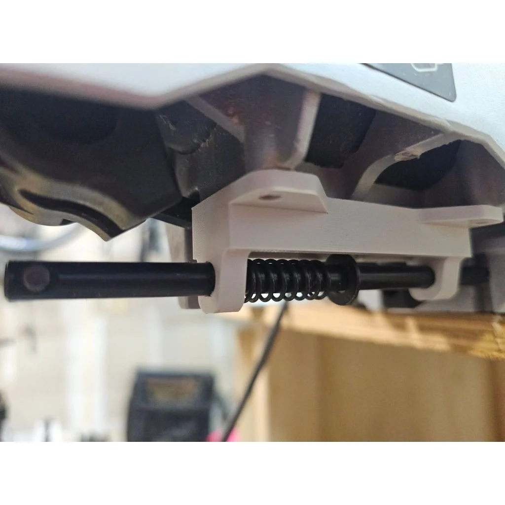 The underside of a miter saw. There's a metal bar sliding into the mentioned plastic piece. A spring can be seen pressing between the plastic and a washer.